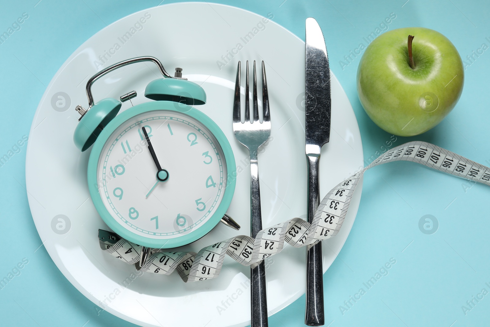 Photo of Alarm clock, apple, measuring tape, plate and cutlery on light blue background, above view