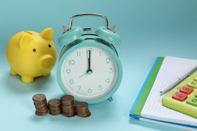 Photo of Alarm clock, coins, piggybank, notebook and calculator on light blue background