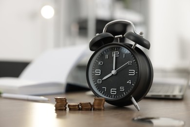 Photo of Alarm clock and coins on wooden desk in office. Space for text