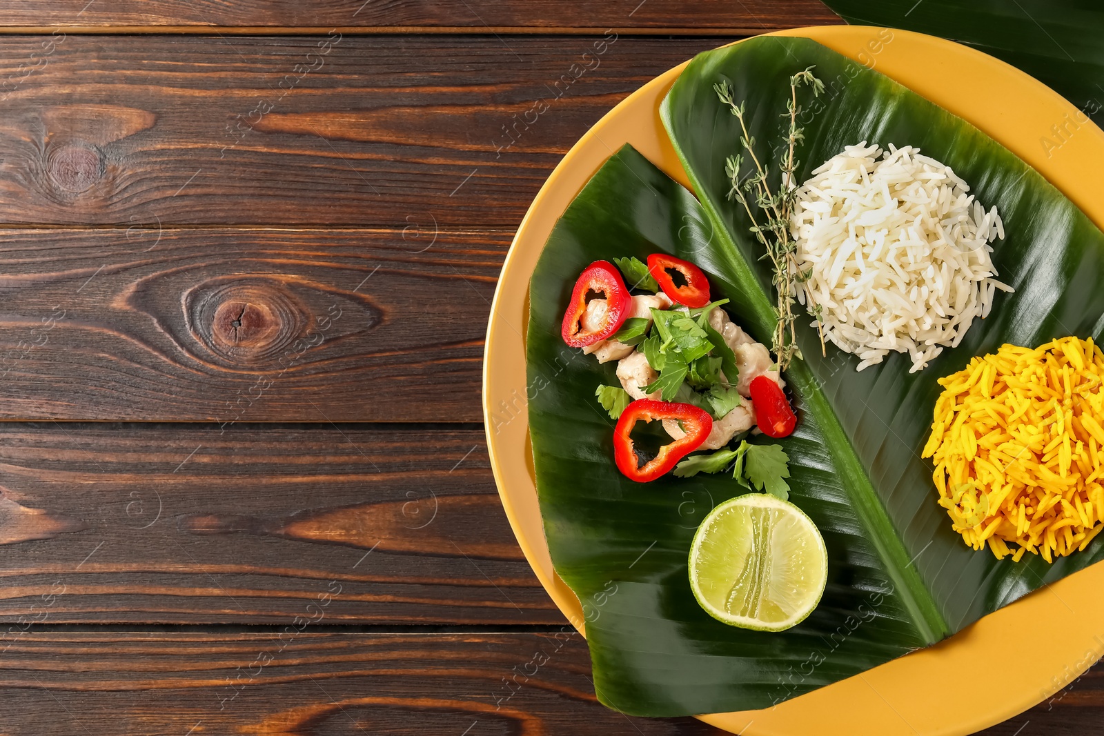 Photo of Cut banana leaf with different food on wooden table, top view. Space for text