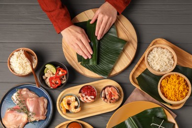 Photo of Woman wrapping food into banana leaf at wooden table with products, top view. Healthy eco serving