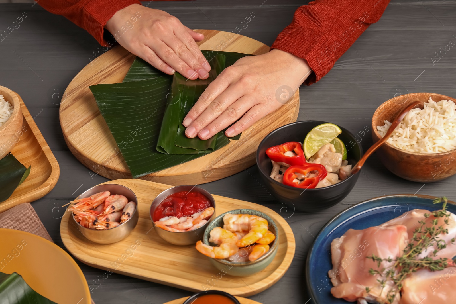 Photo of Woman wrapping food into banana leaf at wooden table with products, closeup. Healthy eco serving