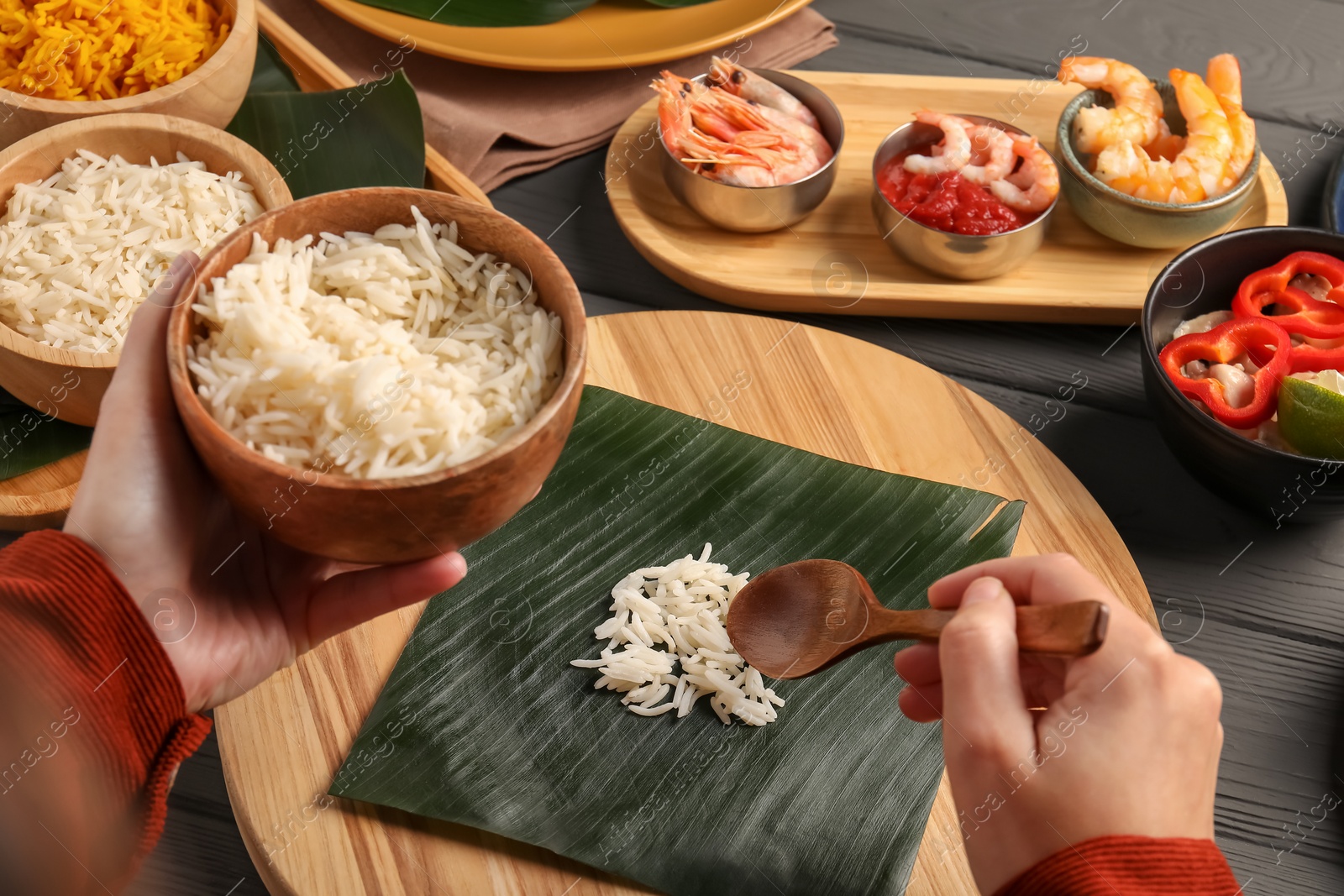 Photo of Woman putting rice onto banana leaf at wooden table with products, closeup