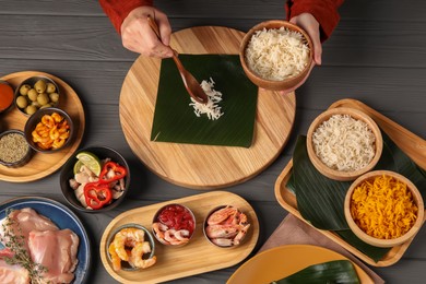 Photo of Woman putting rice onto banana leaf at wooden table with products, top view