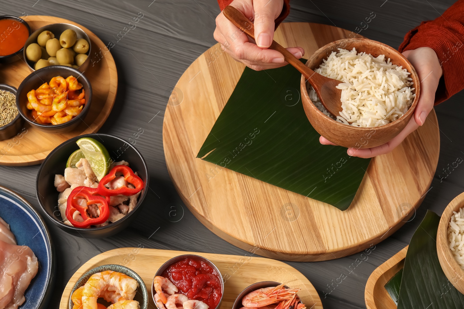 Photo of Woman putting rice onto banana leaf at wooden table with products, above view