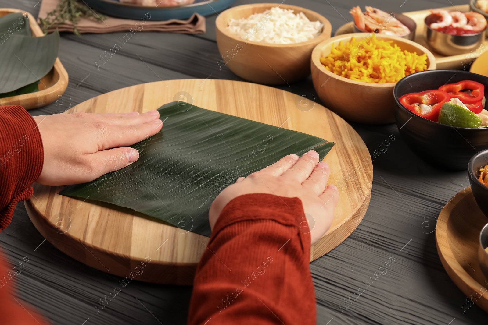 Photo of Woman with banana leaf at wooden table with different products, closeup. Healthy eco serving