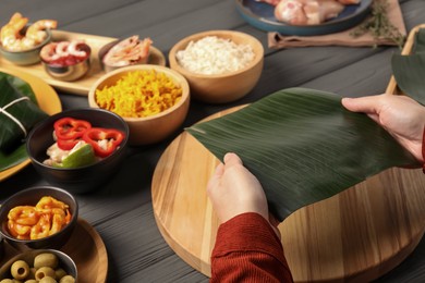 Photo of Woman with banana leaf at wooden table with different products, closeup. Healthy eco serving