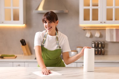 Woman cleaning white marble table with paper towel in kitchen