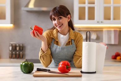 Woman with bell pepper using paper towels at white marble table in kitchen