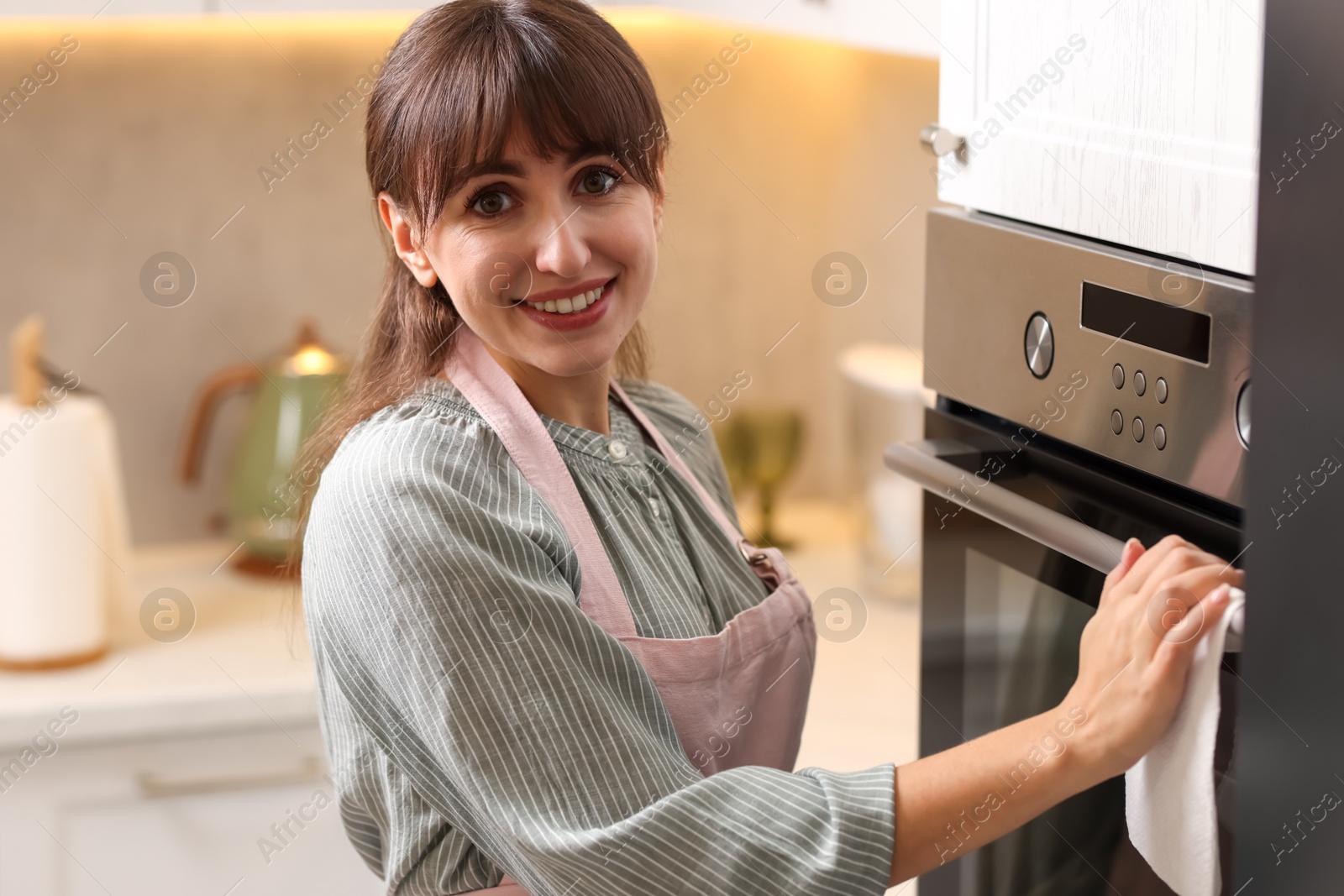 Photo of Smiling woman wiping oven with paper towel in kitchen