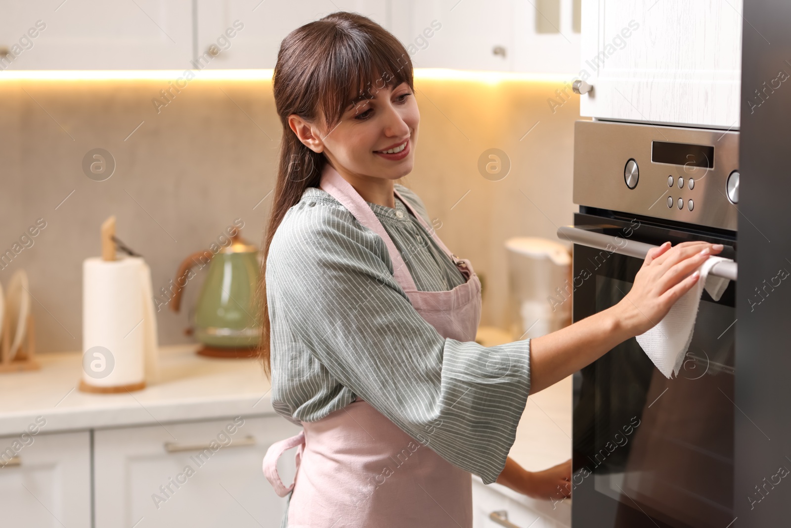 Photo of Smiling woman wiping oven with paper towel in kitchen