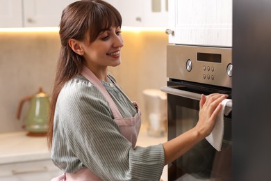 Smiling woman wiping oven with paper towel in kitchen