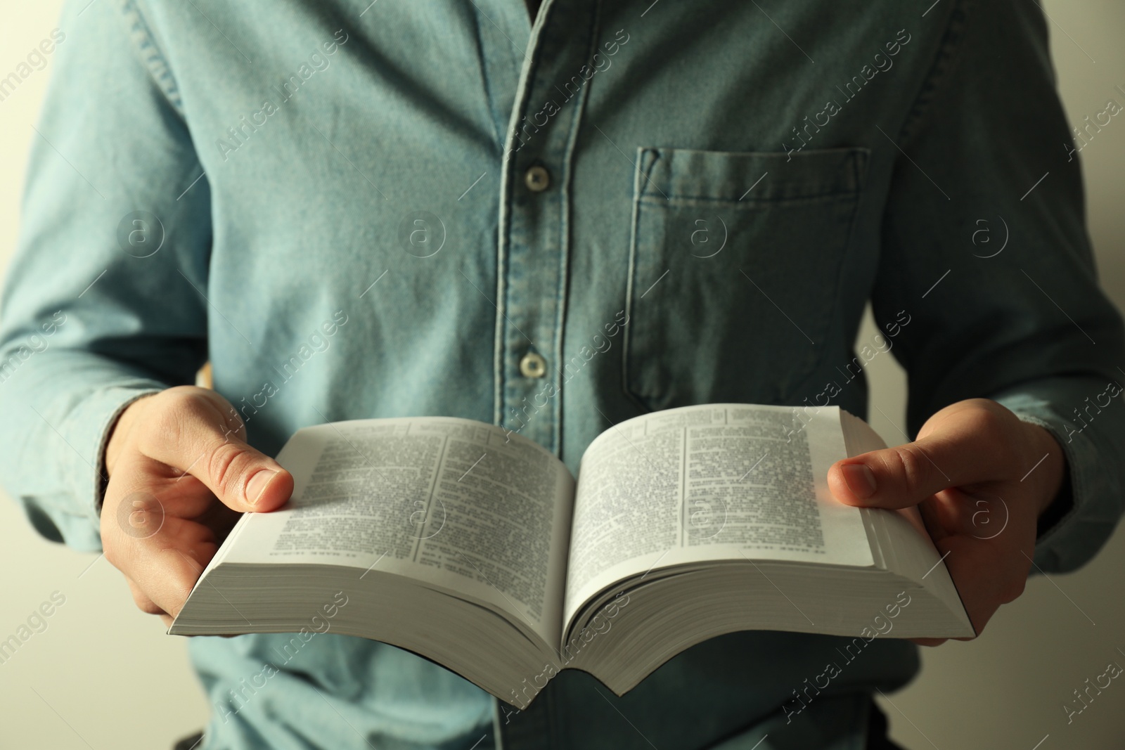 Photo of Man reading Holy Bible in English language on light background, closeup