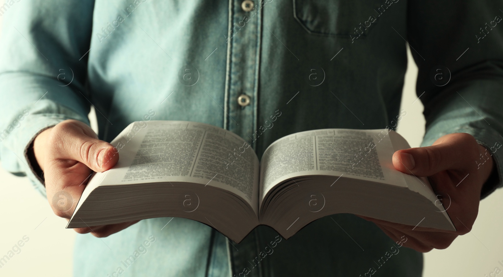 Photo of Man reading Holy Bible in English language on light background, closeup