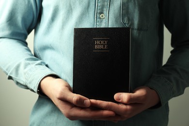 Photo of Man with hardcover Holy Bible on light background, closeup