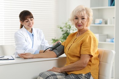 Doctor measuring senior woman's blood pressure during appointment in hospital