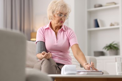 Senior woman writing results of blood pressure measurement at home