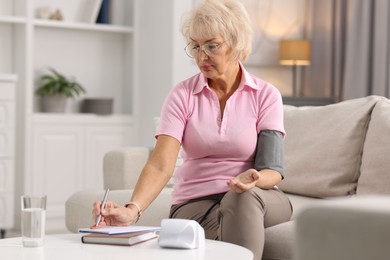 Senior woman writing results of blood pressure measurement at home