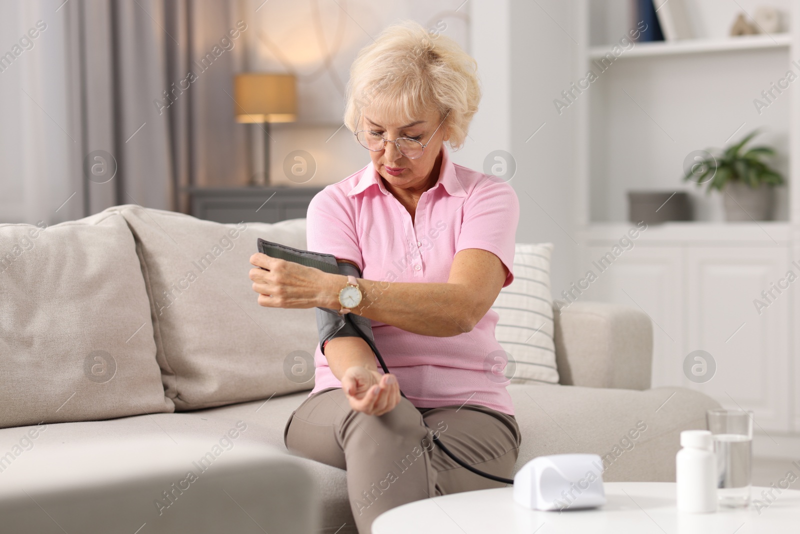 Photo of Senior woman measuring blood pressure on sofa at home