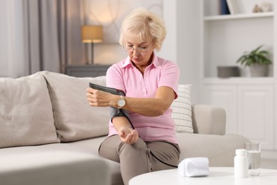 Senior woman measuring blood pressure on sofa at home