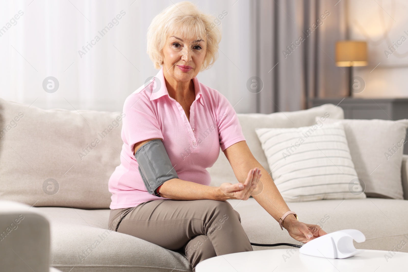 Photo of Senior woman measuring blood pressure on sofa at home