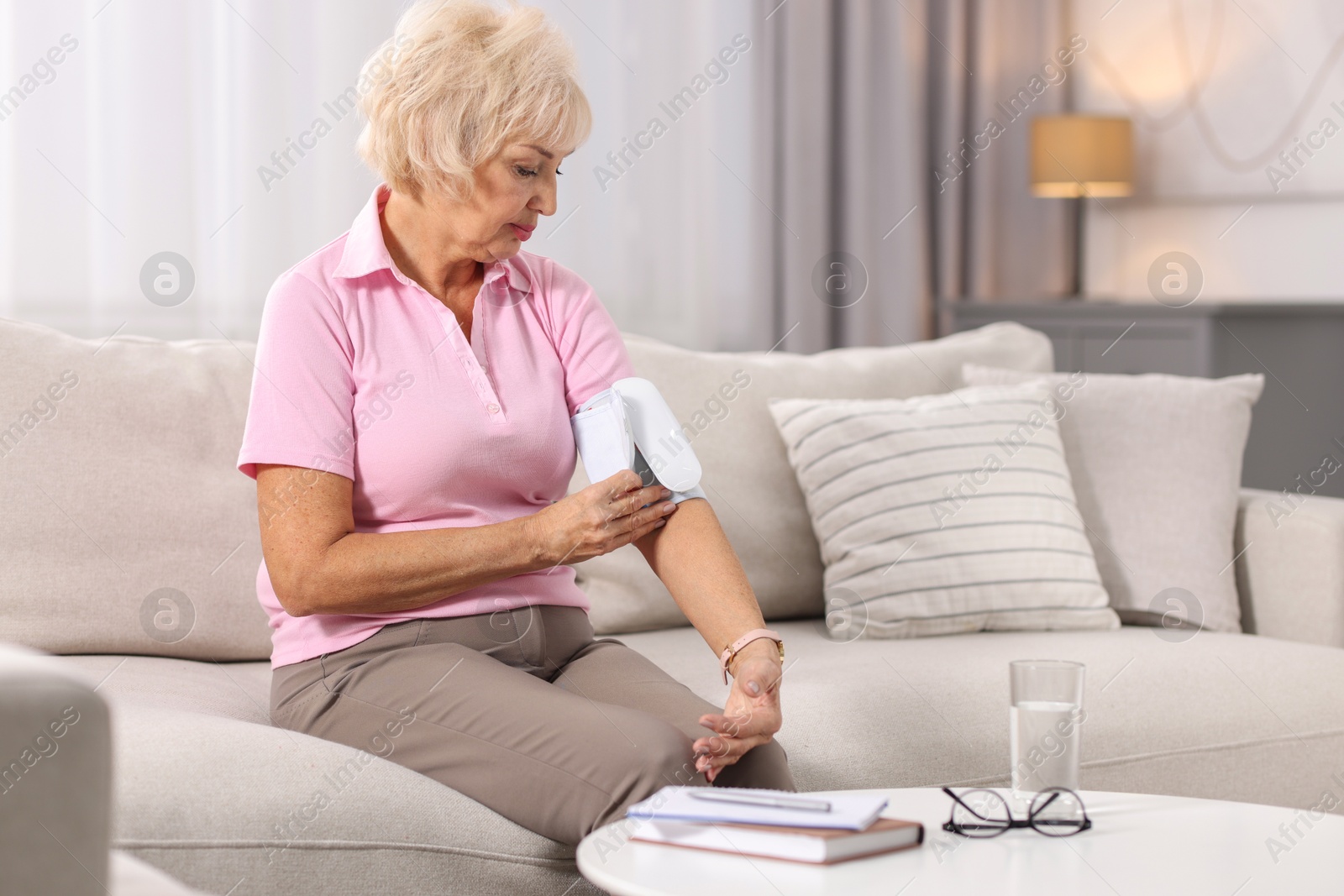 Photo of Senior woman measuring blood pressure on sofa at home. Space for text