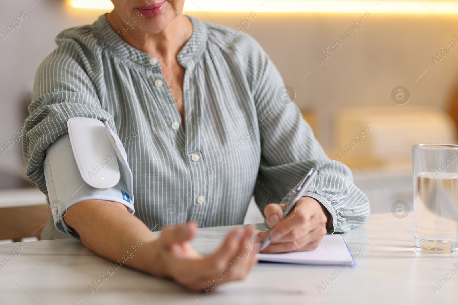 Photo of Senior woman writing results of blood pressure measurement in kitchen at home, closeup