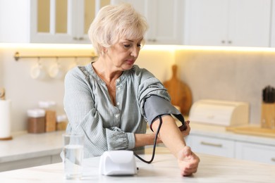 Senior woman measuring blood pressure at table in kitchen