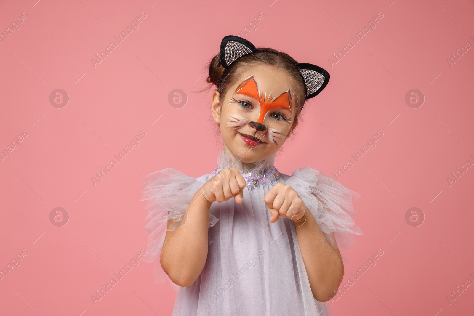 Photo of Cute girl with painted face and ears as cat on pink background