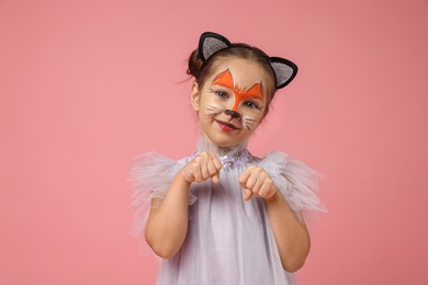 Cute girl with painted face and ears as cat on pink background