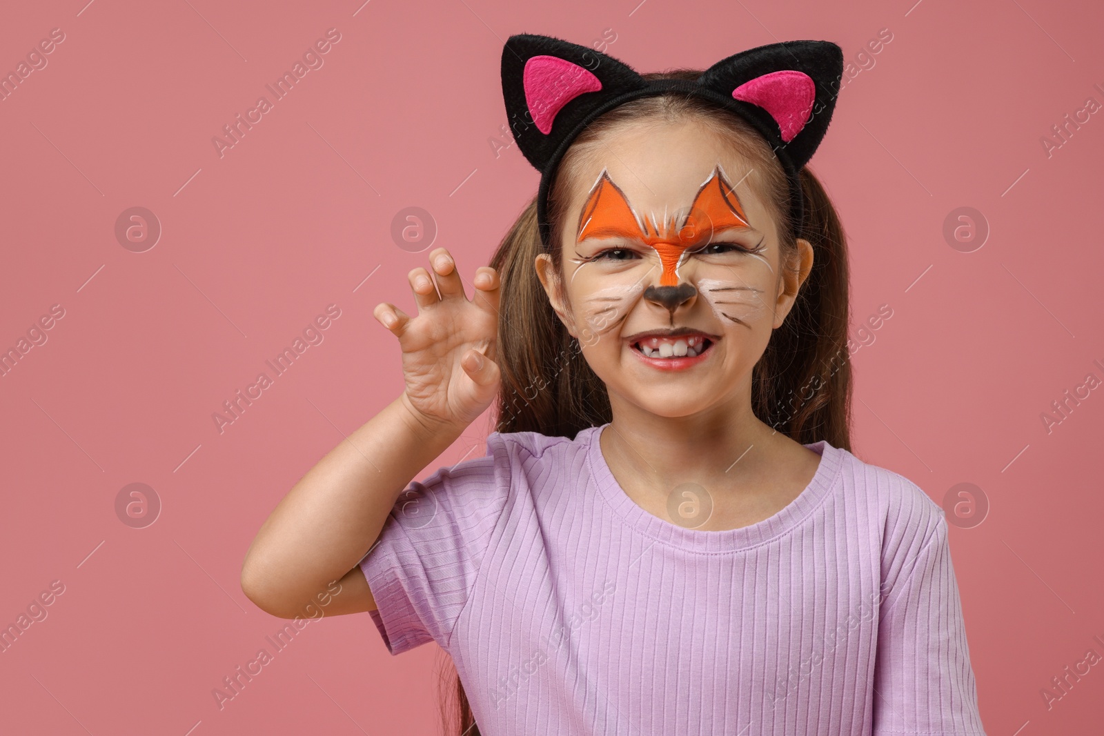 Photo of Cute girl with painted face and ears as cat on pink background