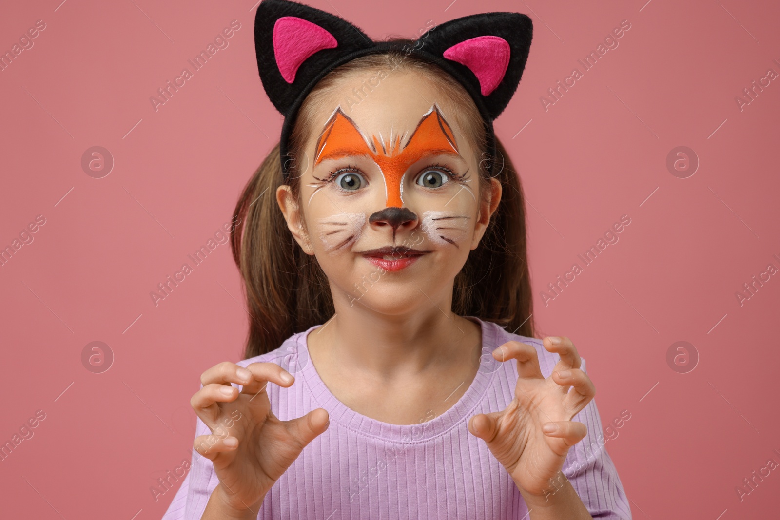 Photo of Cute girl with painted face and ears as cat on pink background