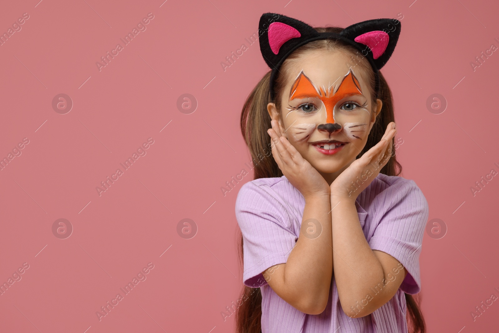 Photo of Cute girl with painted face and ears as cat on pink background, space for text