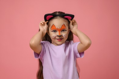 Cute girl with painted face and ears as cat on pink background