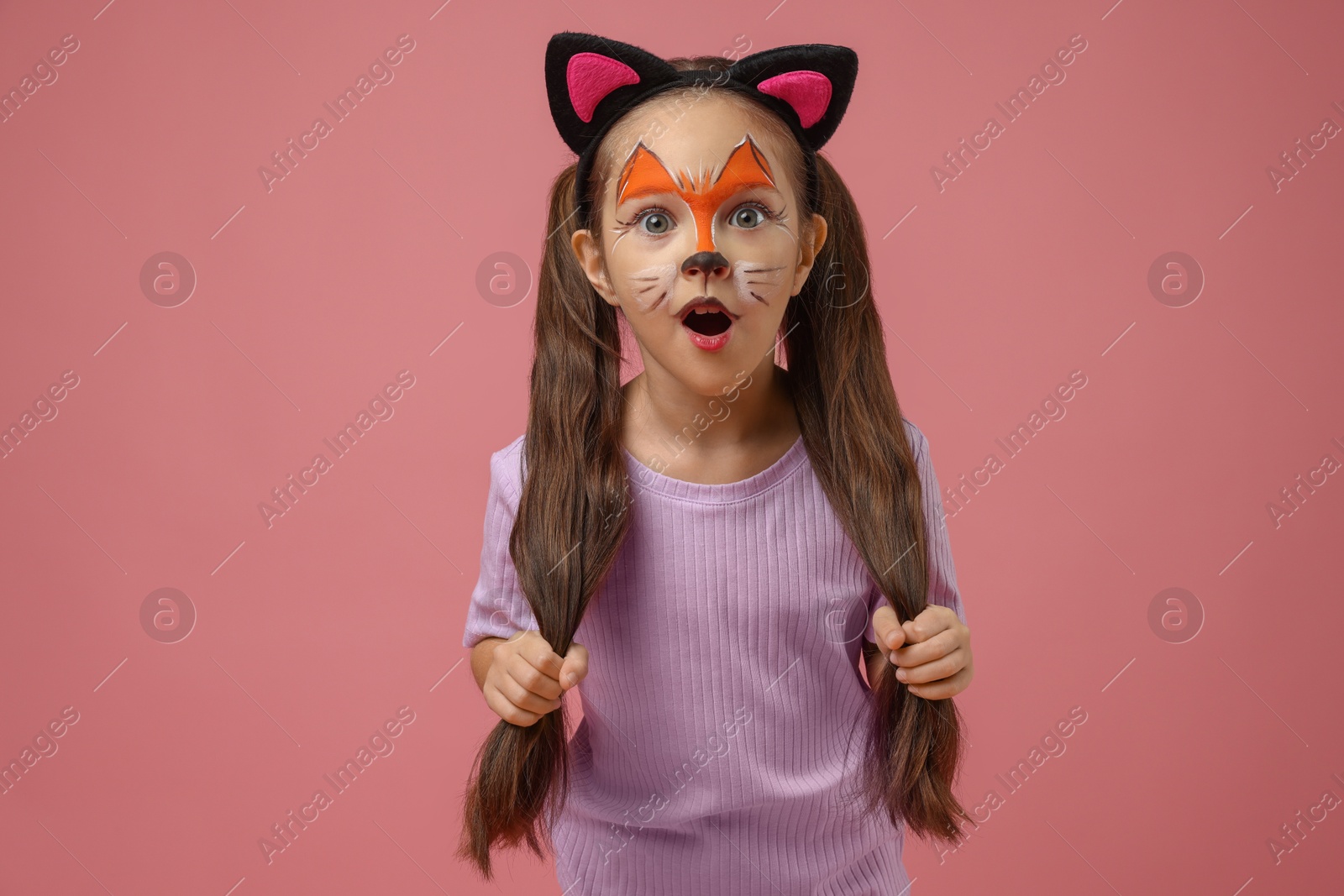 Photo of Cute girl with painted face and ears as cat on pink background