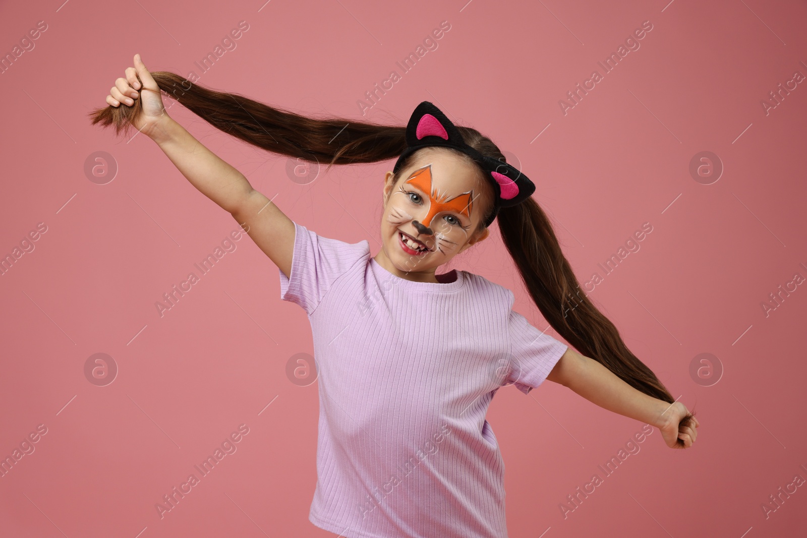 Photo of Cute girl with painted face and ears as cat on pink background