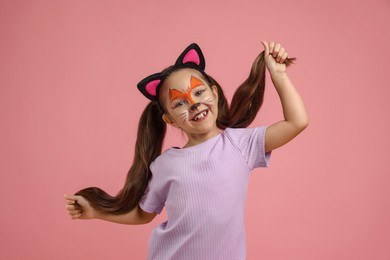 Photo of Cute girl with painted face and ears as cat on pink background