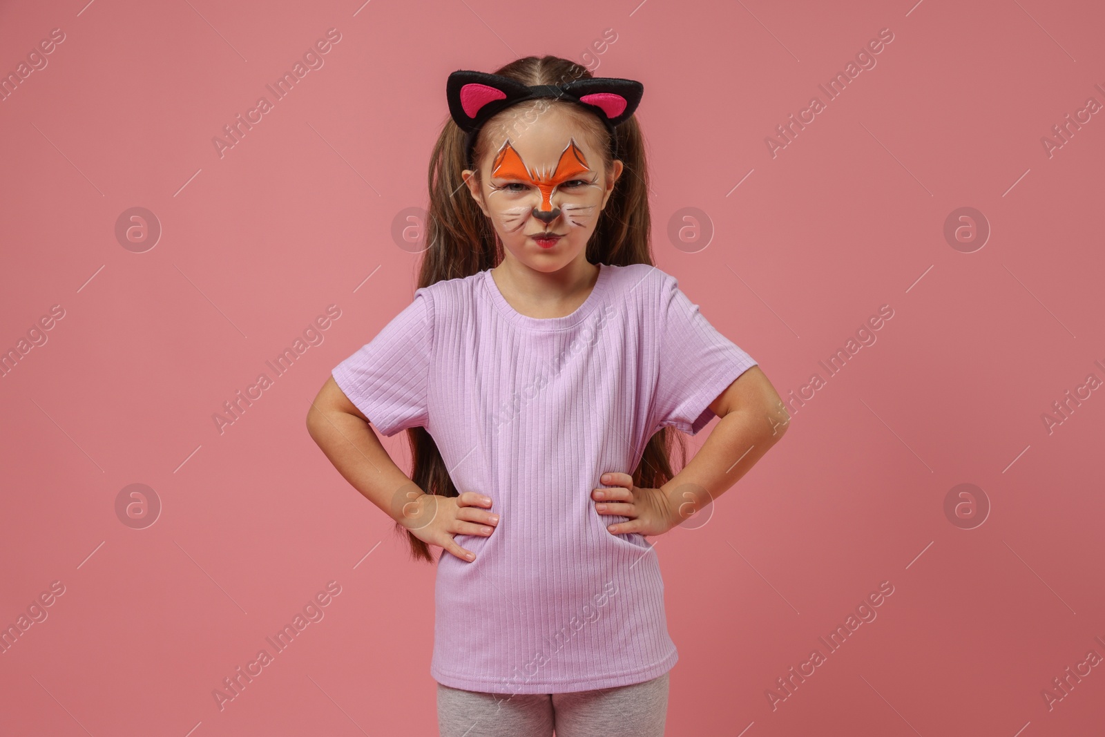 Photo of Cute girl with painted face and ears as cat on pink background