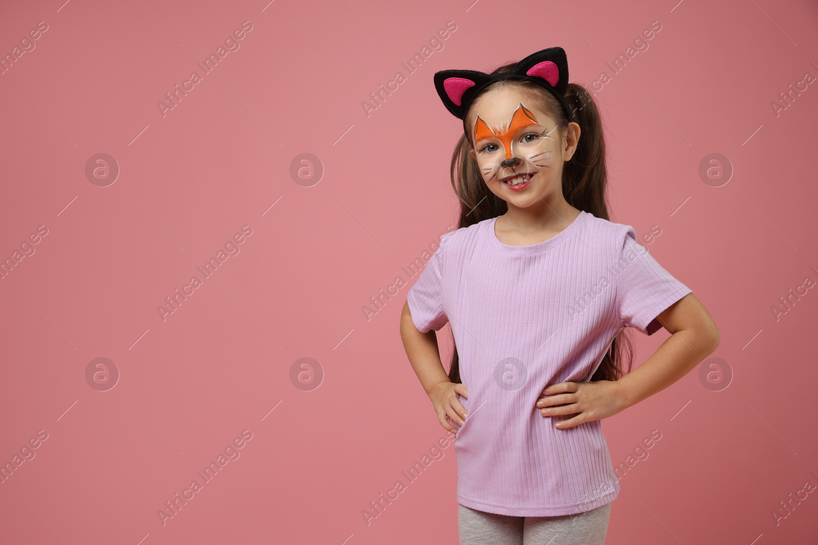 Photo of Cute girl with painted face and ears as cat on pink background, space for text