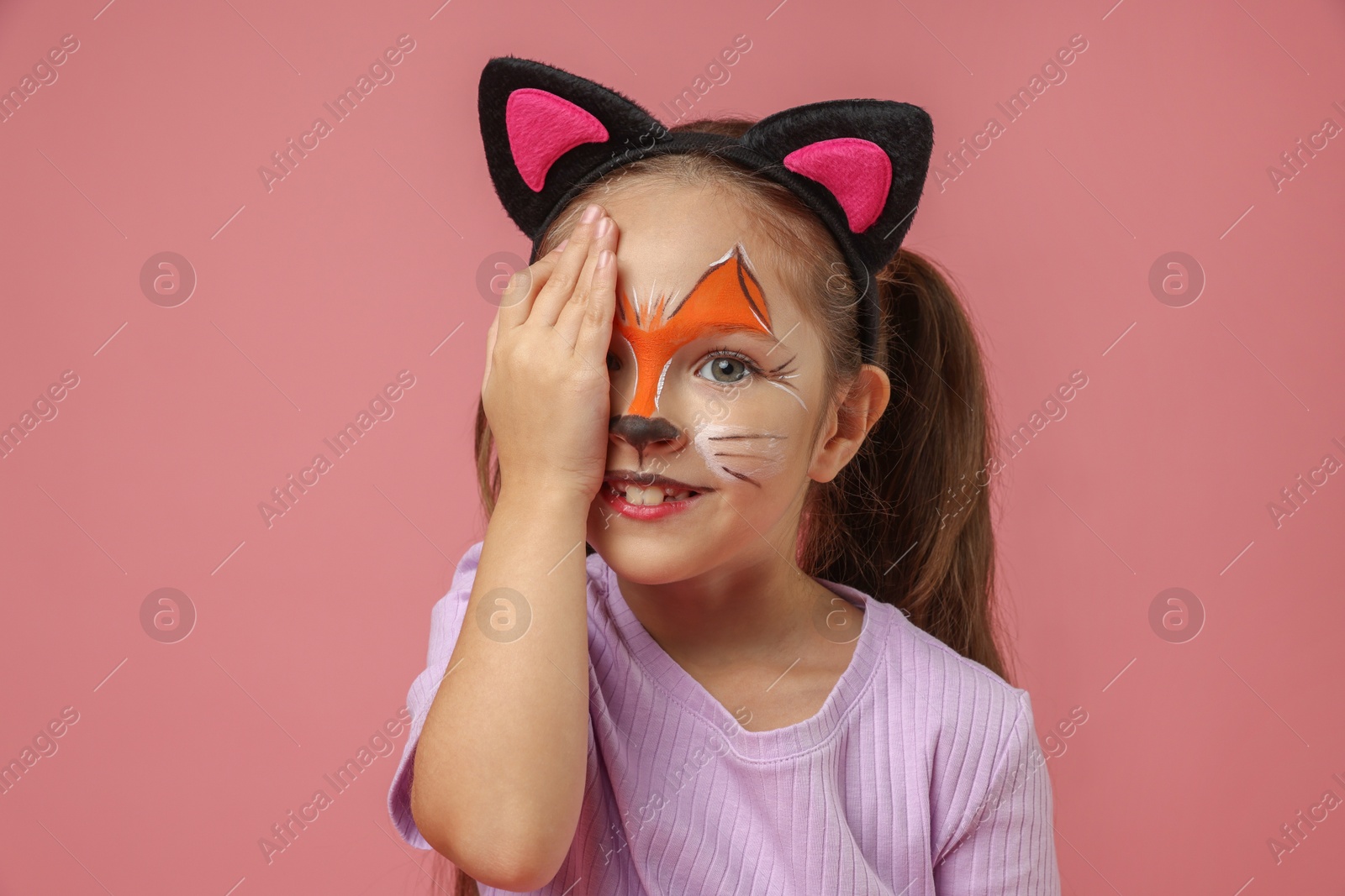 Photo of Cute girl with painted face and ears as cat on pink background