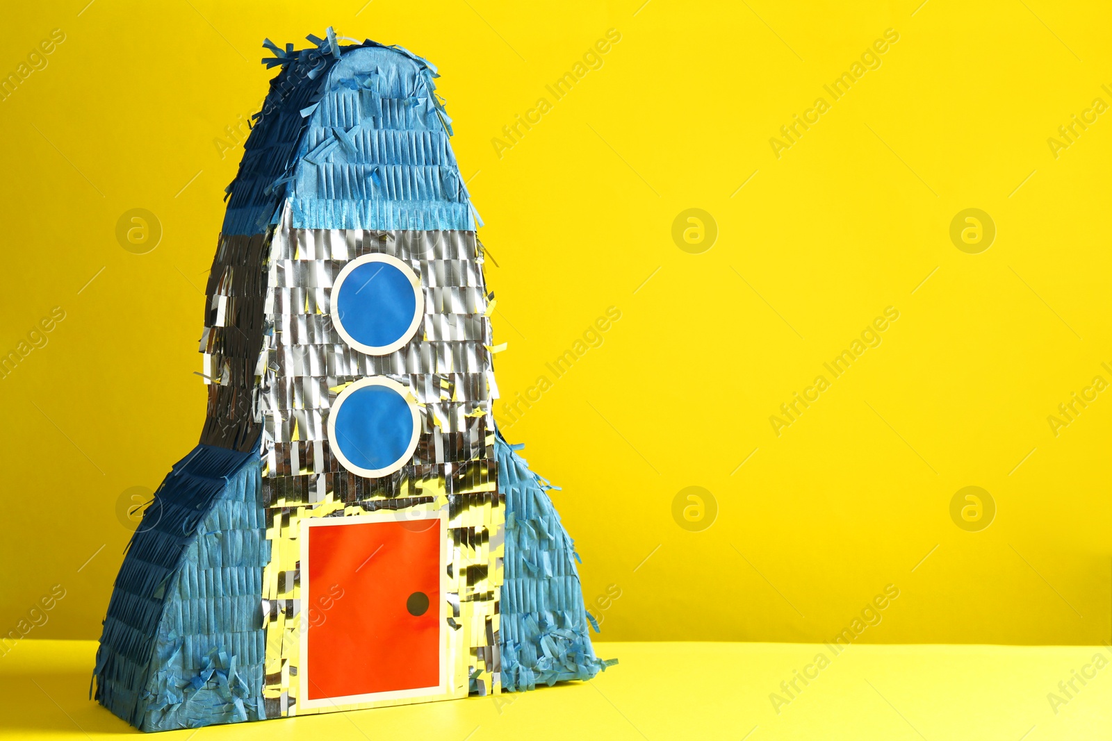 Photo of Bright pinata in shape of spaceship on yellow background. Space for text