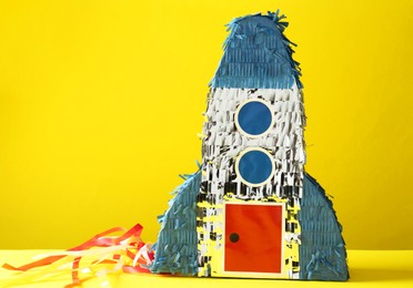 Photo of Bright pinata in shape of spaceship on yellow background. Space for text