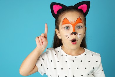 Cute girl with painted face and ears as cat on light blue background