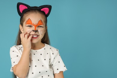 Cute girl with painted face and ears as cat on light blue background, space for text