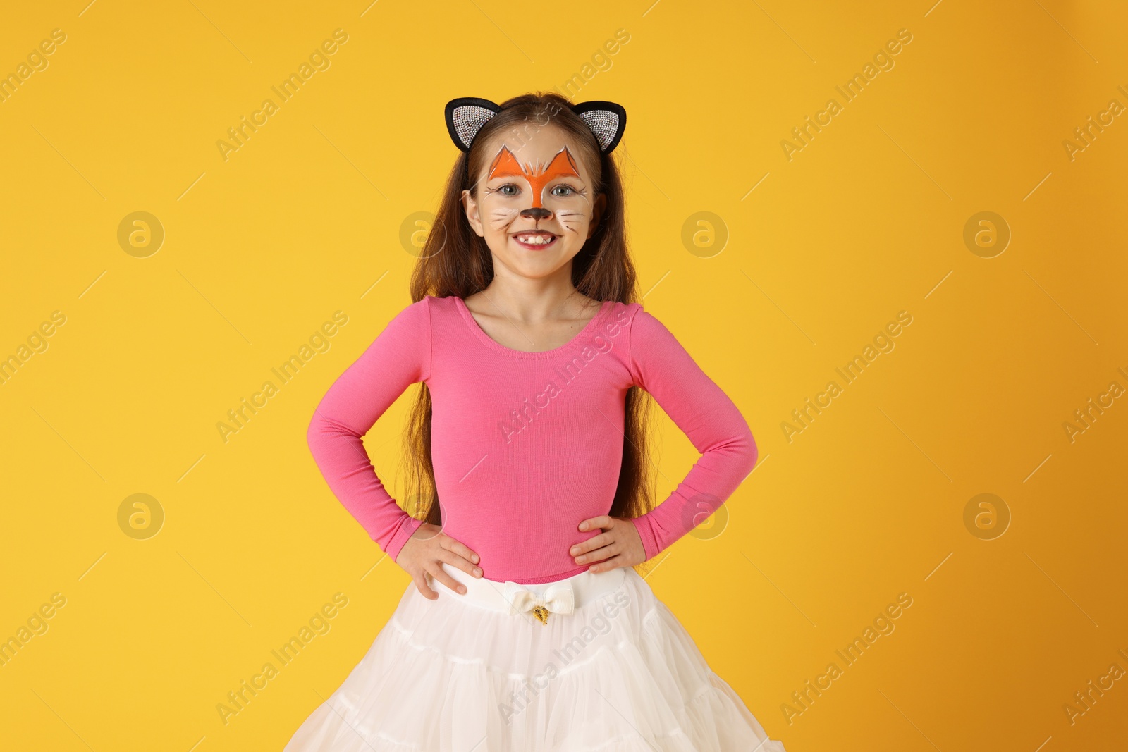 Photo of Cute girl with painted face and ears as cat on orange background