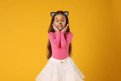 Cute girl with painted face and ears as cat on orange background