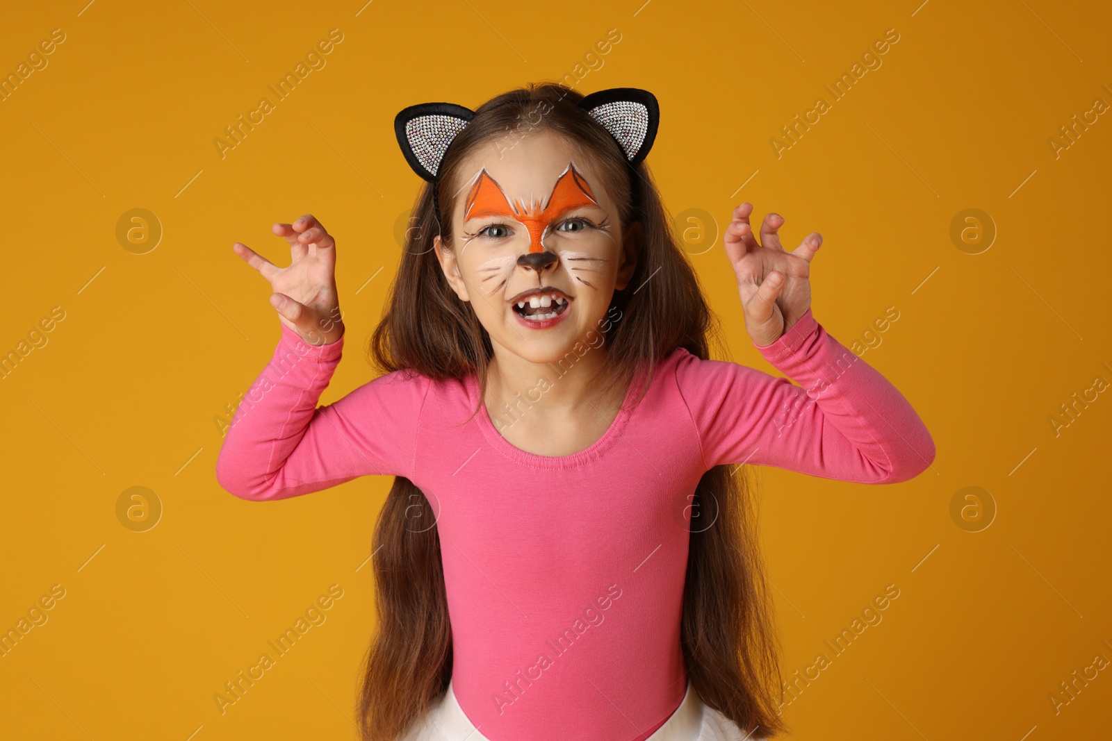 Photo of Cute girl with painted face and ears as cat on orange background