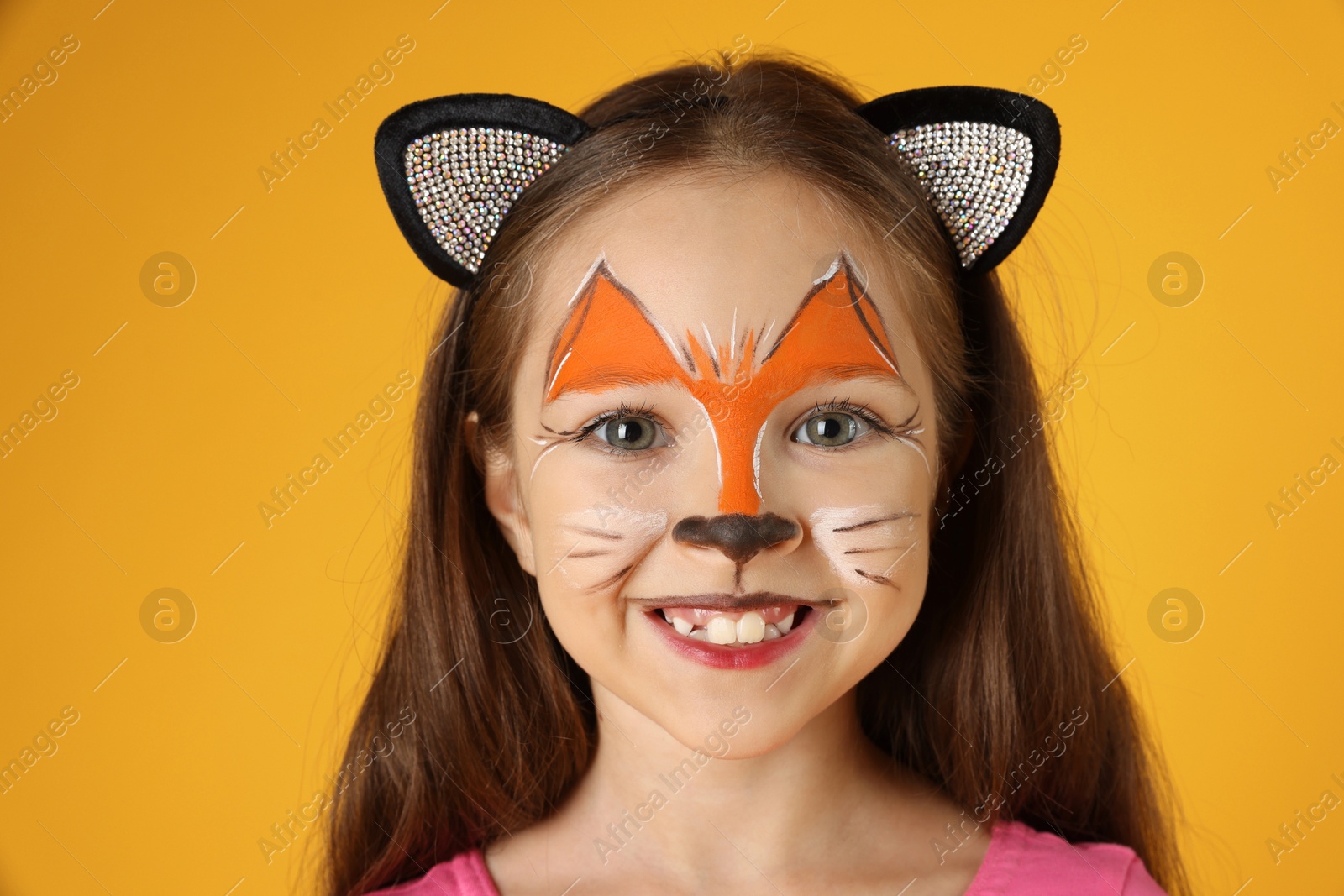 Photo of Cute girl with painted face and ears as cat on orange background