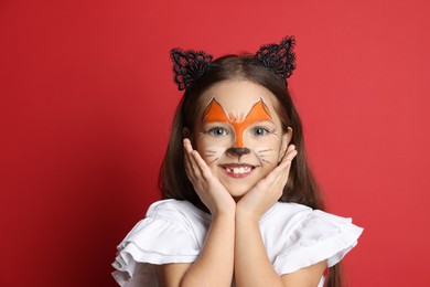 Cute girl with painted face and ears as cat on red background