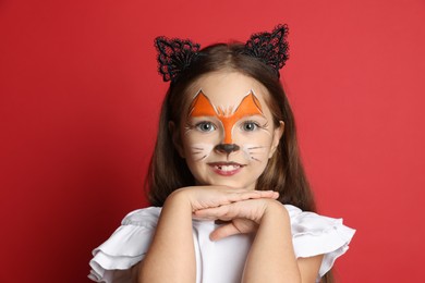 Cute girl with painted face and ears as cat on red background